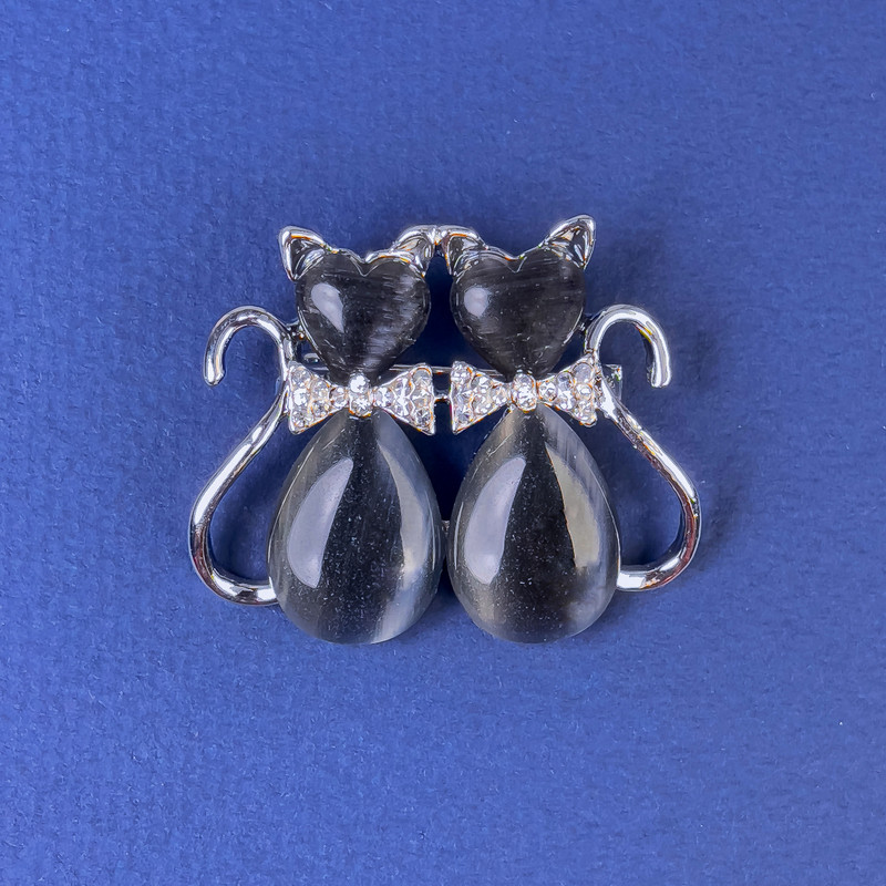 Brooch 'Cats' with dark gray cat's-eye stone, white crystals, silver-toned metal, diameter 31x38 mm +